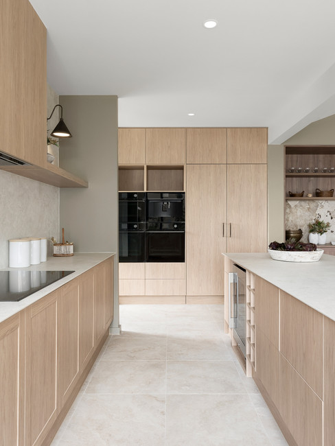 Modern kitchen with light wood cabinets, large island, and stools. Black accents, greenery by window, and neutral tones create a calm mood.