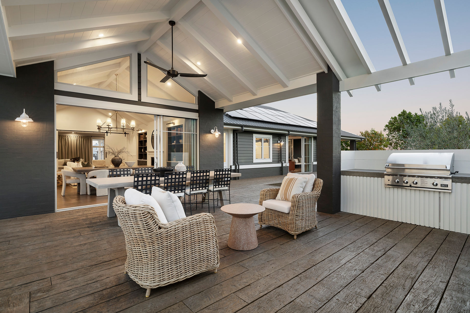 Outdoor living area with cathedral ceiling. Two whicker armchairs with small round side table and large outdoor dining table with black metal dining chairs.