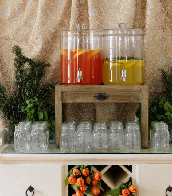 Two jugs with orange and yellow beverages behind empty glasses