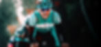 An athlete cyclist facing front with a dark background and green fitted clothes with a green helmet and black glasses