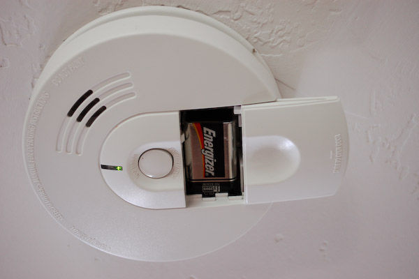 Smoke detector with battery plate pulled back showing battery: You've worked hard to buy your first home. Make sure that you protect that home by replacing batteries on your smoke alarms and carbon monoxide detectors regularly
