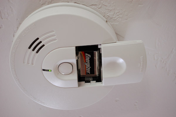 Smoke detector with battery plate pulled back showing battery: You've worked hard to buy your first home. Make sure that you protect that home by replacing batteries on your smoke alarms and carbon monoxide detectors regularly