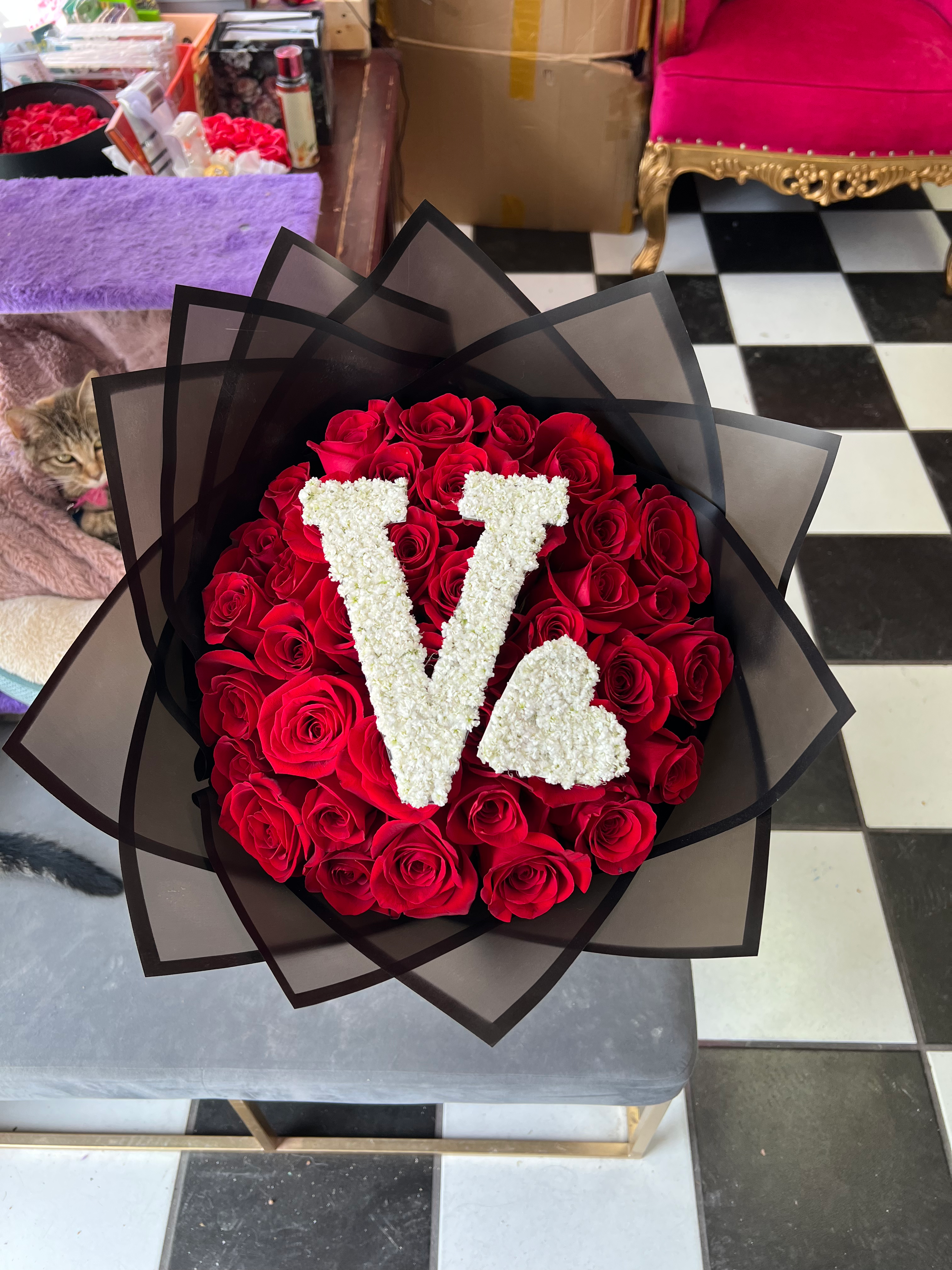 Red rose bouquet in black wrap with decorative initial and heart on top.