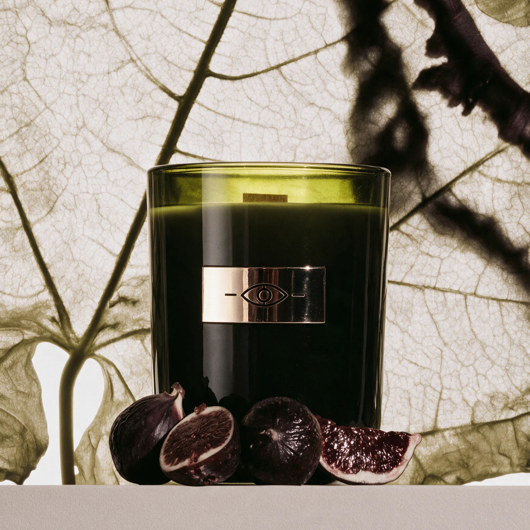 Smoked Fig candle in olive glass with gold eye plaque and fresh figs.