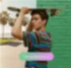 A man holding a skateboard. Half of the background shows a skate park, and half shows a green brick wall, demonstrating the change background tool.