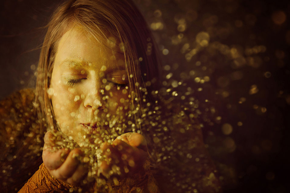 Mädchen pustet in goldenden Glitzerstaub 