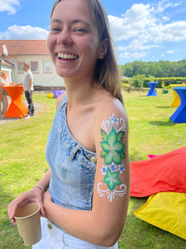Glimlachende vrouw met groene bloemen en witte sierdetails geschilderd op haar bovenarm.