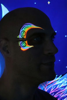 Profiel van een man met kleurrijke neon facepaint rond het oog, oplichtend onder blacklight