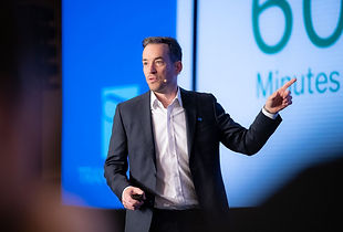 A man in a suit gestures to a screen during a presentation