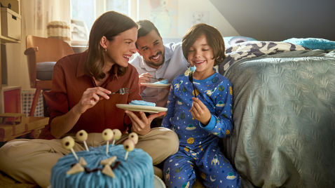 Familie im Schlafanzug mit blauer Alien-Torte auf dem Bett – Setfotografie zur Thermomix-TM7-Kampagne, Andreas Reimann