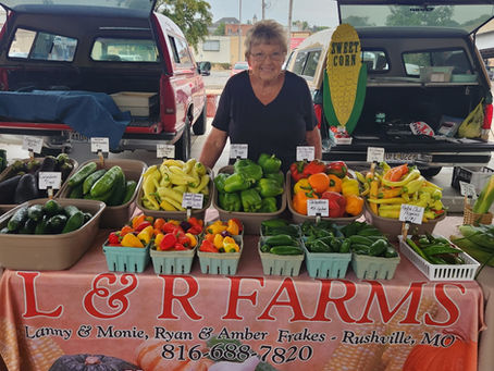A smiling woman standing behind a table covered with baskets of various types of produce