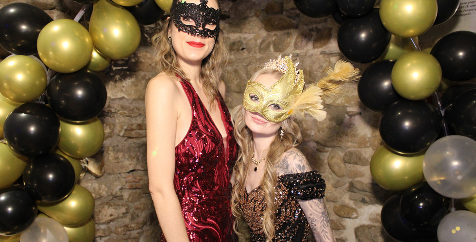 deux amies devant une arche de ballons noir et or portant des masques à l'occasion d'une soirée bal masqué