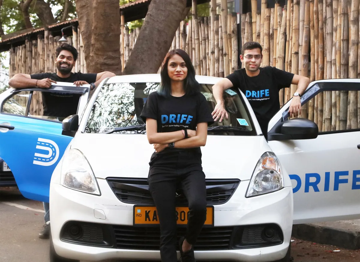 3-people-stand-at-a-car-with-the-drife-logo-on-it-smiling-at-the-camera.webp