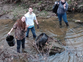 teens in a shallow creek removing an old tire and trash