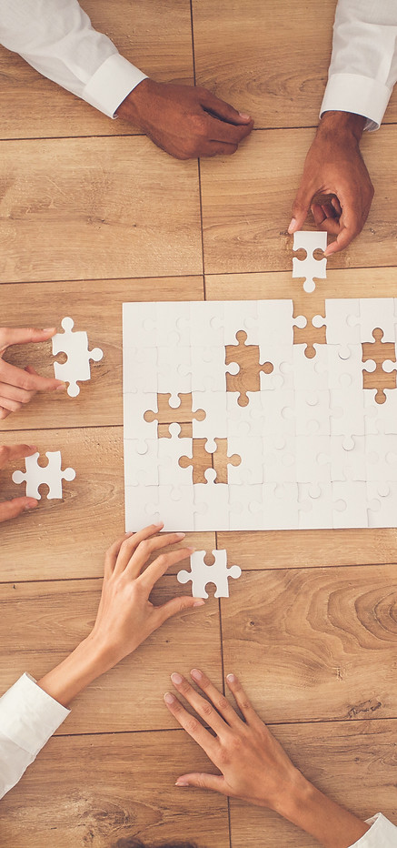 Tisch mit weissen Puzzleteilen und mehreren Händen die es zusammensatzen