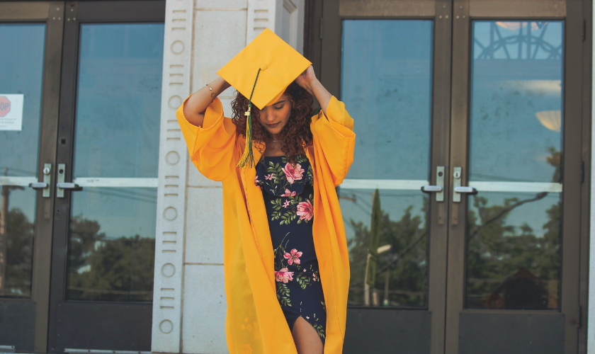 girl in yellow graduation gown preparing to put her cap on