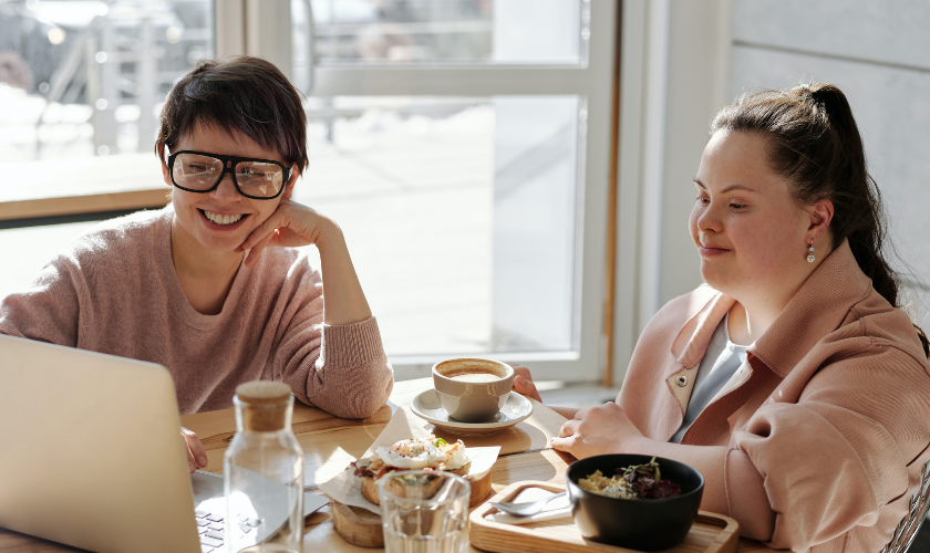 a woman with glasses sitting with a girl with down syndrome at computer