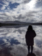 A walker admiring the still loch and mountains in the distance during a low level hike