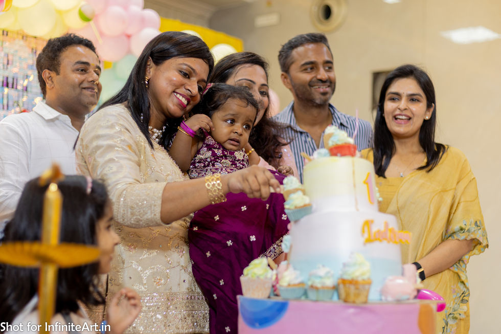 The entire family on stage - mother, father, birthday girl--held in her mother's arms, and aunts and uncles, as they cut the birthday cake; candid image captured during a baby's first birthday party
