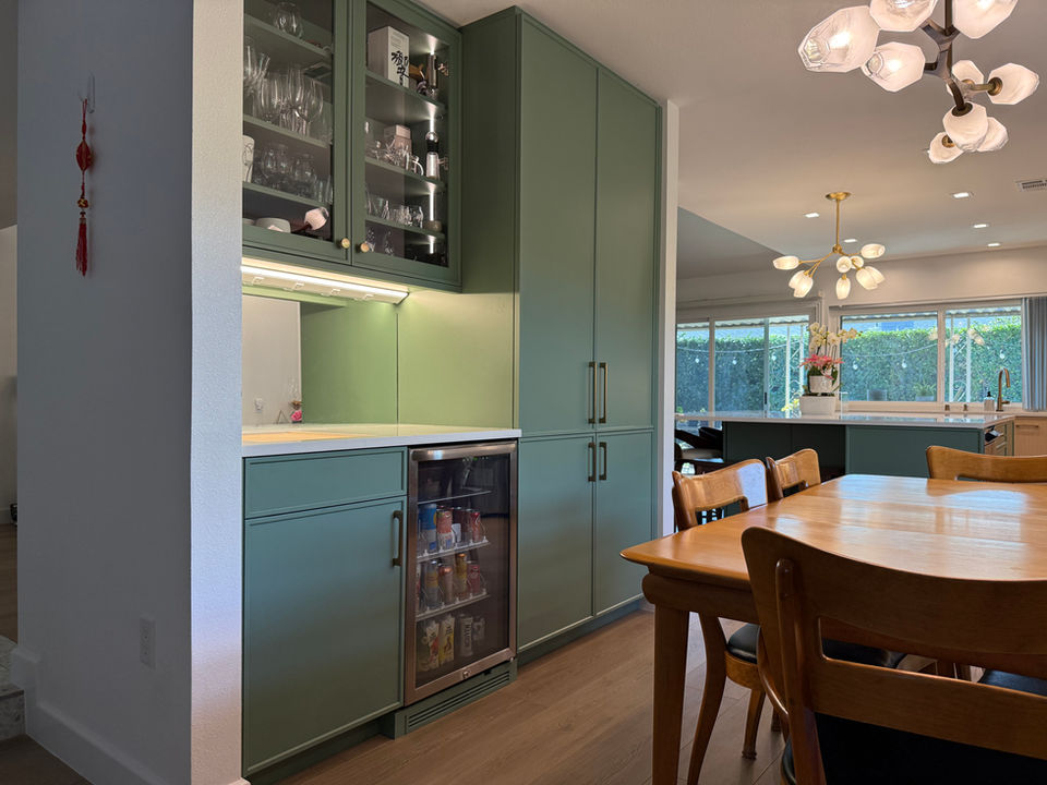 Green cabinetry with a refrigerator and glass display. A dining room setting.