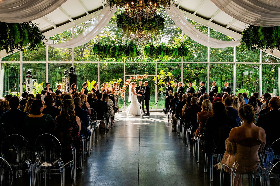A wedding ceremony set in a modern Dutch greenhouse, styled with foliage chandeliers and ceiling draping, surrounded by lush greenery.