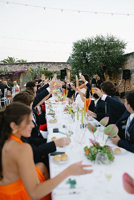 Guests toasting at a long imperial table during an outdoor wedding dinner in a traditional Italian setting.