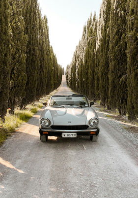 Vintage Italian car driving through a classic cypress-lined road in the Tuscan hills, perfect for a romantic destination wedding.