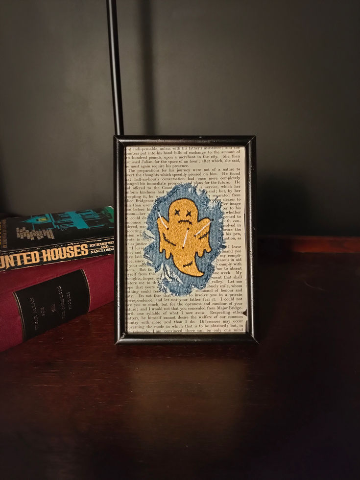 black frame, old book page, frayed denim patch, light-brown voodoo ghost with stitched features and white pins stuck in it.