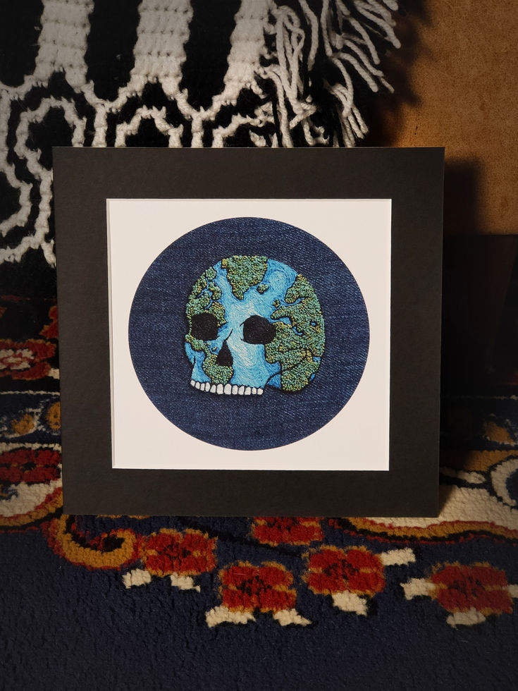 circular denim print, white and black square mount, skull shaped planet earth, blue stitched seas, textured green islands