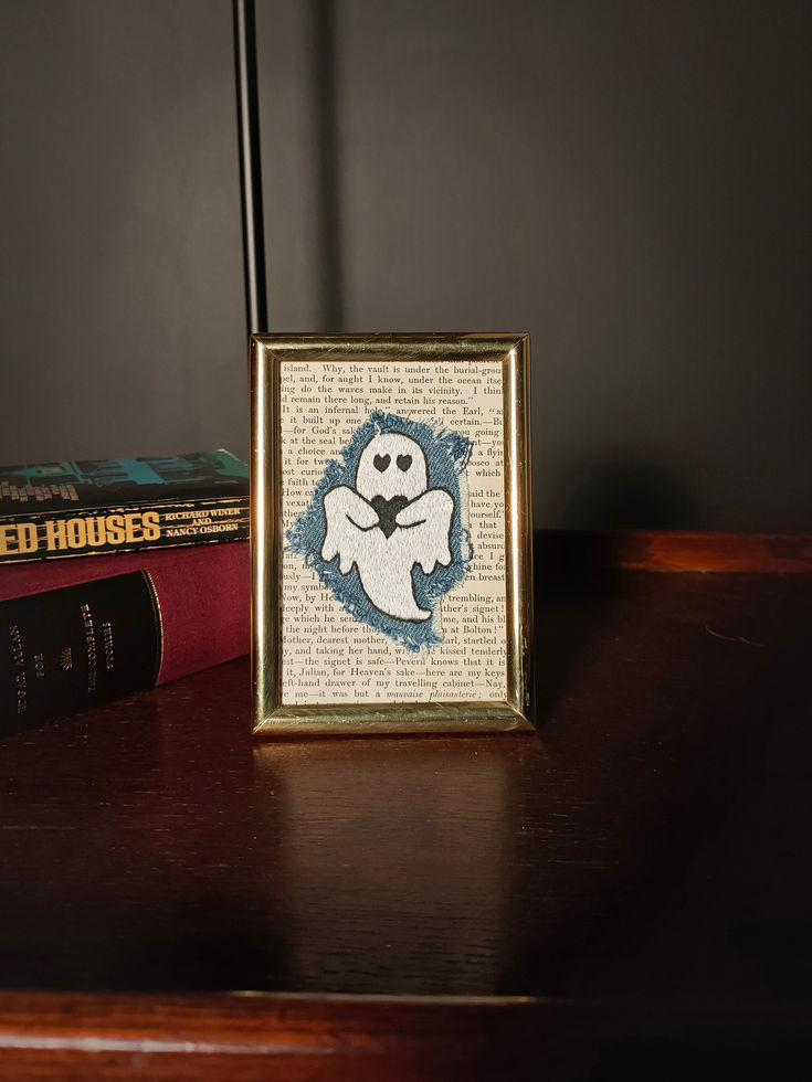 brass framed mixed media art - antique book page, frayed denim patch, white embroidered ghost with black hearts