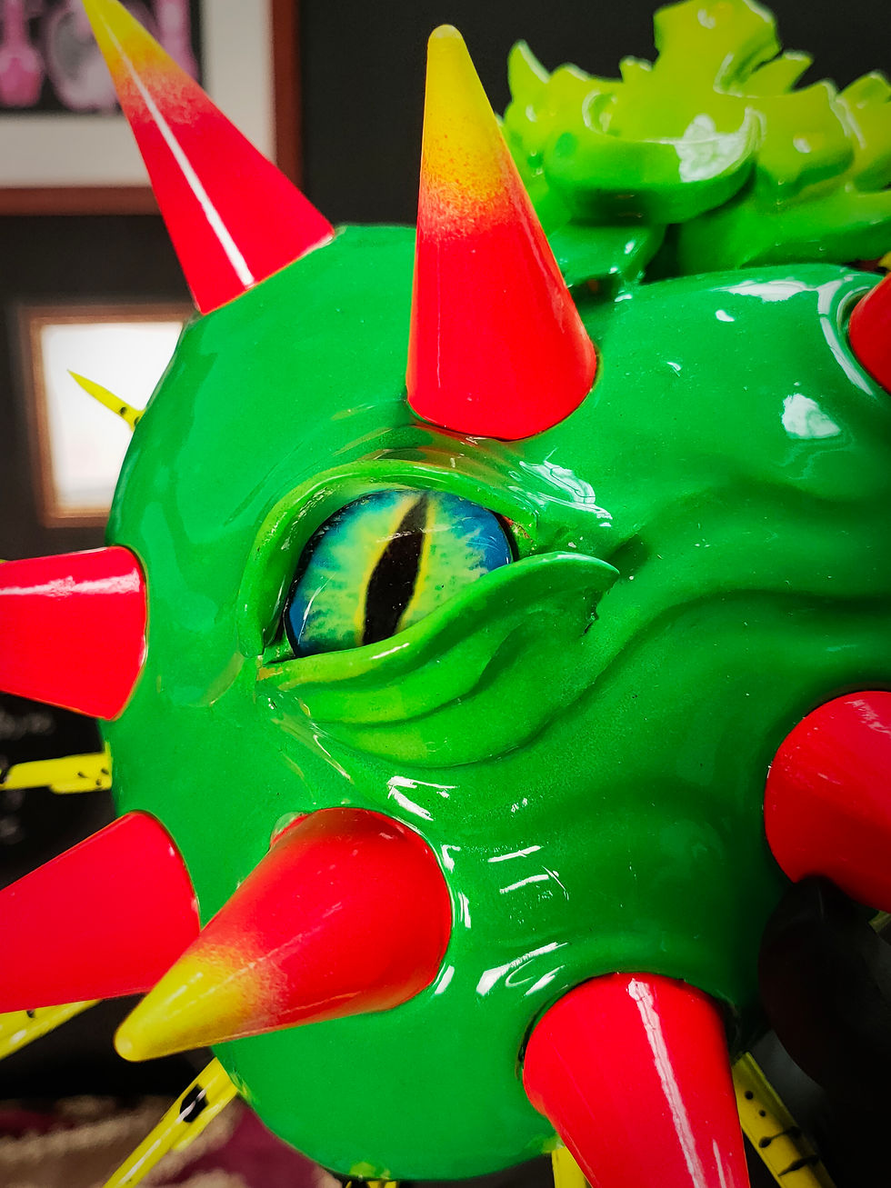 close up view of green eye in vibrant green sacred heart sculpture with orange and yellow conical spikes.