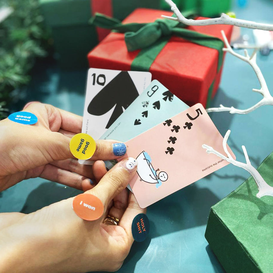 Woman's hands holding playing cards with numbers; Christmas gift in the background.