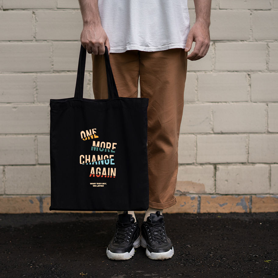 Person holding a black tote bag with "ONE MORE CHANGE AGAIN" text on it.
