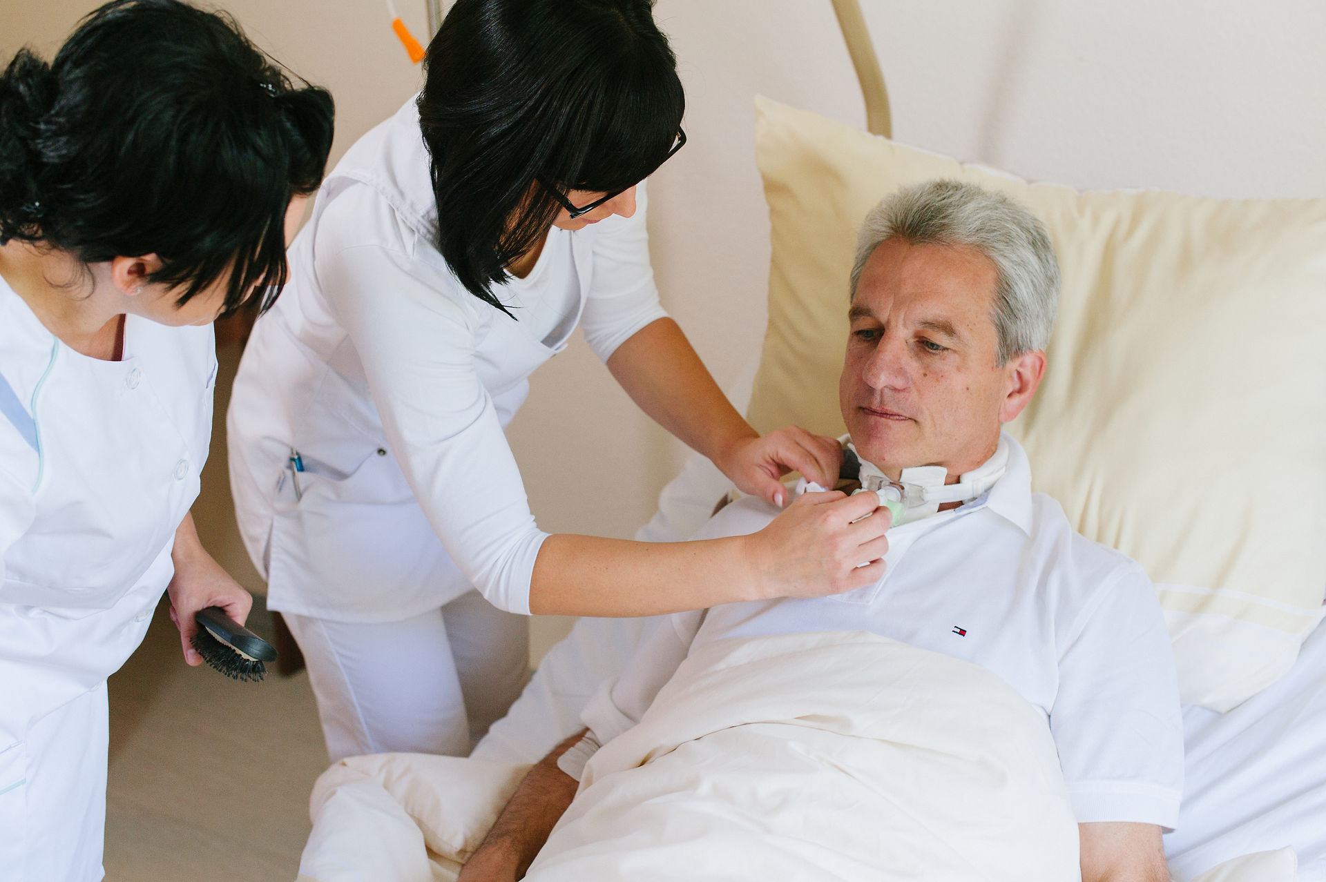 Krankenschwester befestigt Gerät zur Beatmung am Hals eines männlichen Patienten mit grauem Haar