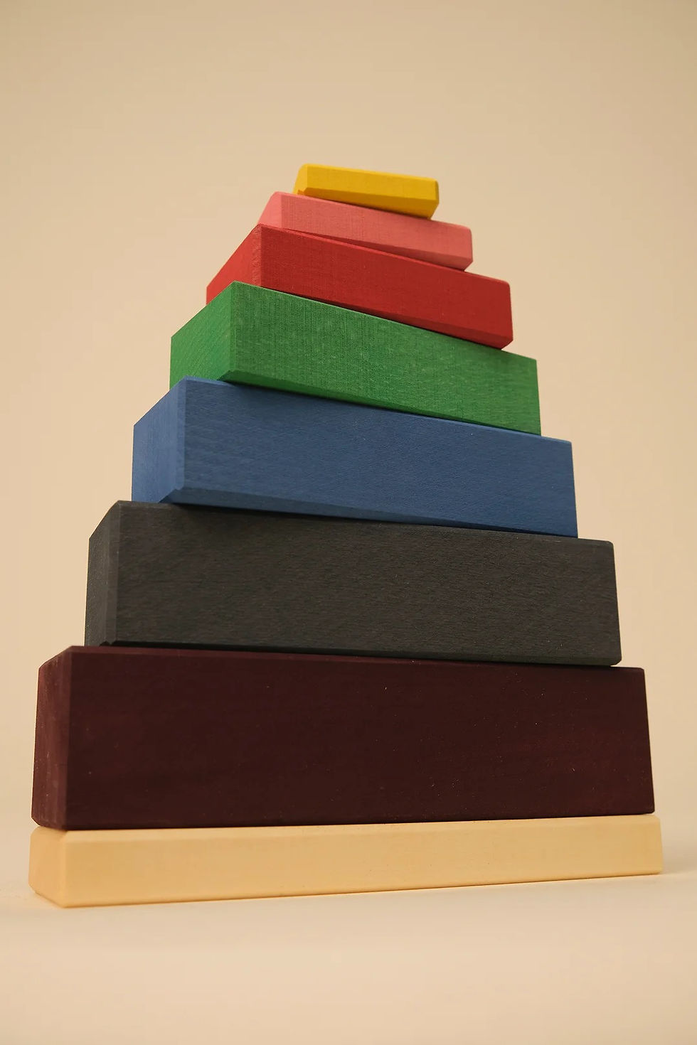 TOYTO wooden blocks stacking tower arranged as a neat 7 color pyramid on a light beige surface.