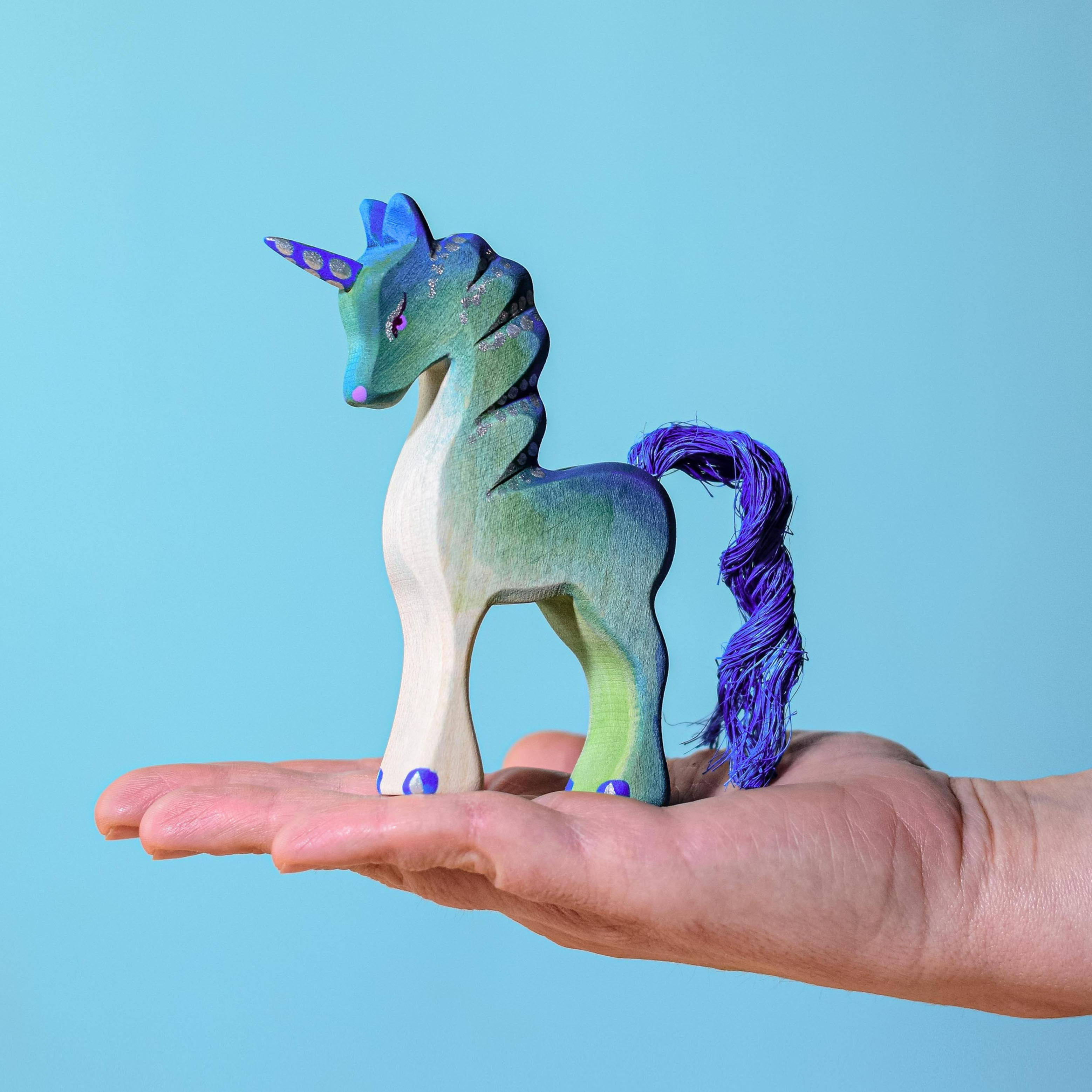 A hand holding the Bumbu Toys Handmade Wooden Baby Unicorn-Green
