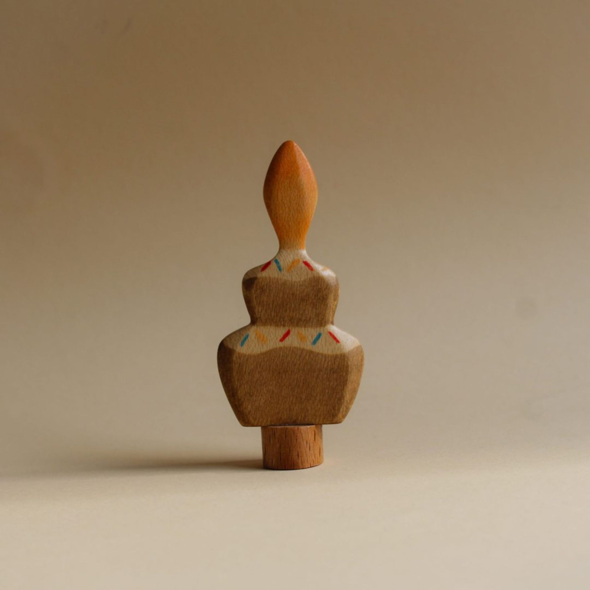 Juharka wooden cake ornament with two tiers, hand-painted sprinkles, and a wooden flame, standing in a natural wooden base.