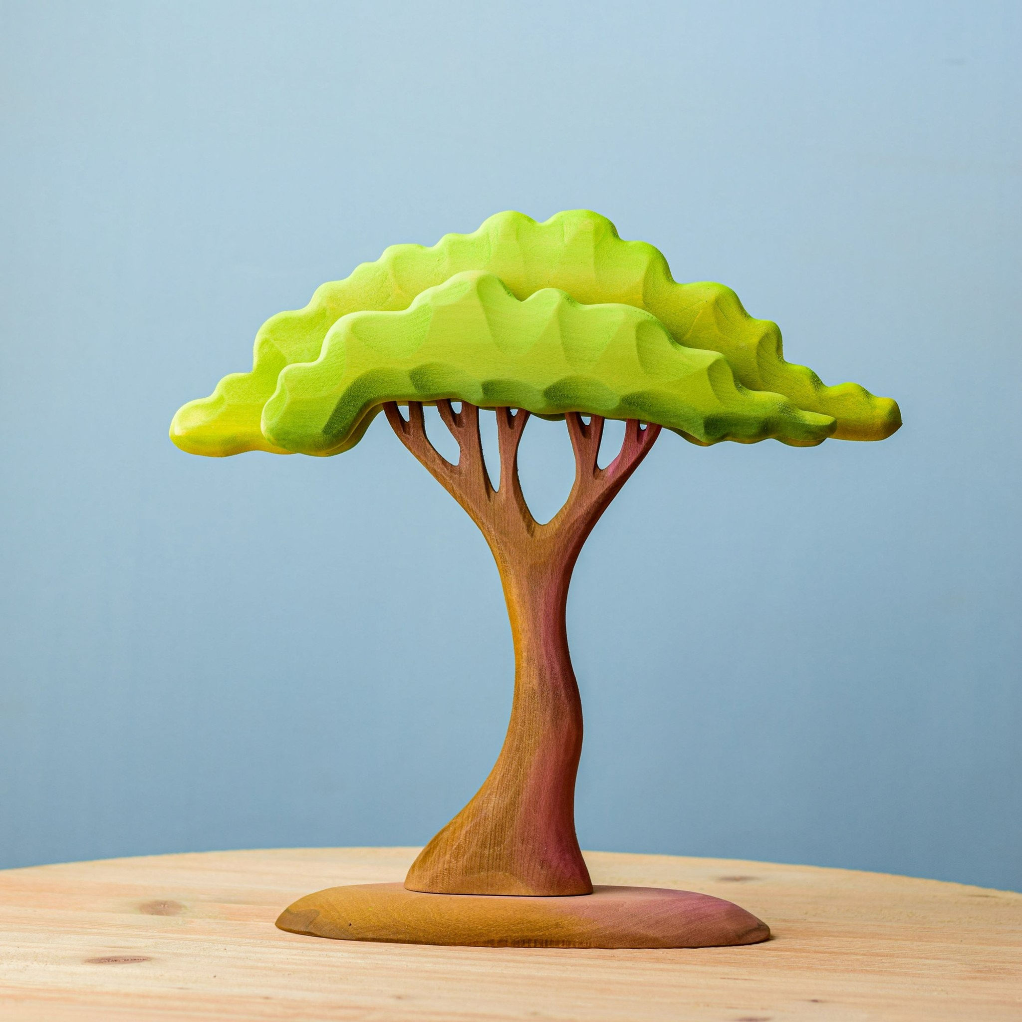Handcrafted wooden large acacia tree toy surrounded by wooden lion family and foliage on a wooden table by Bumbu Toys