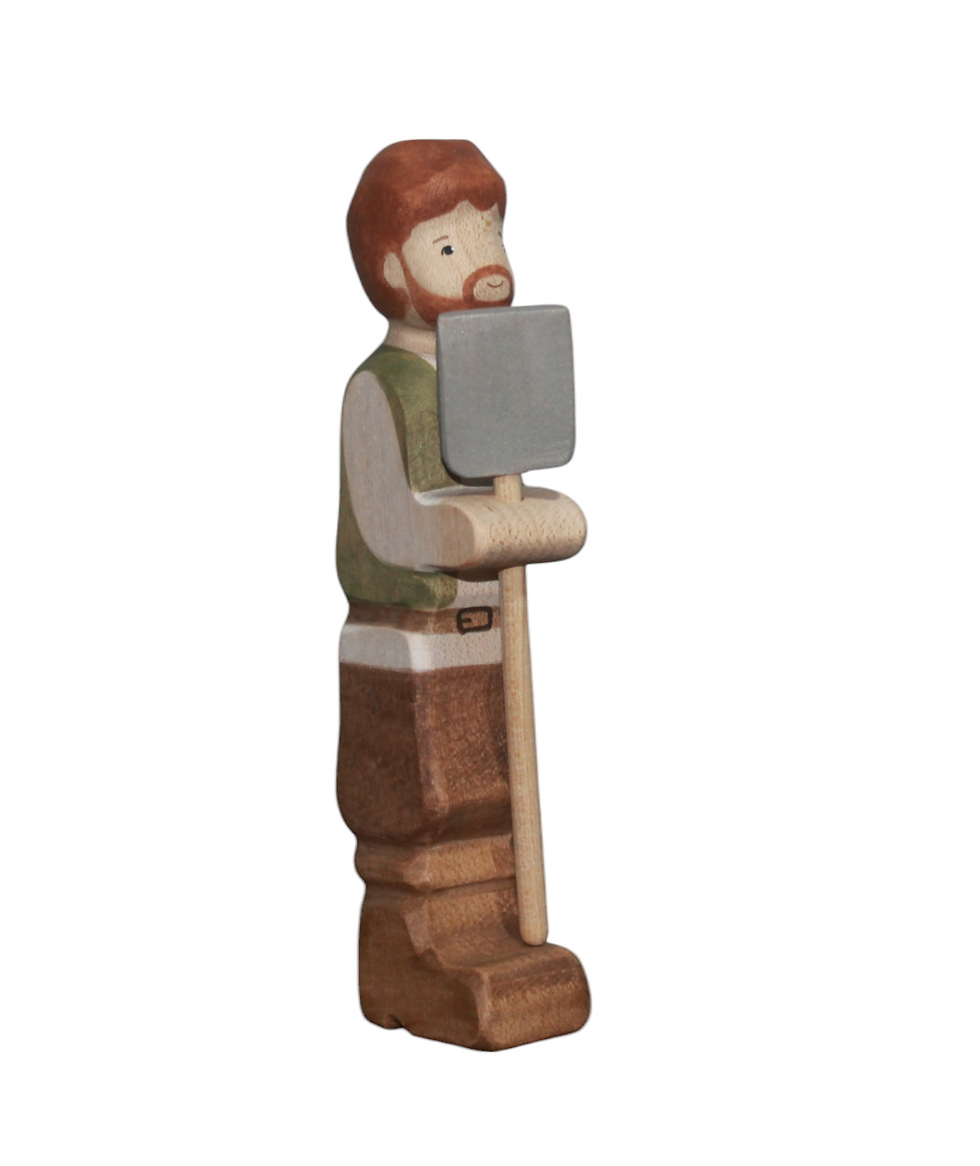 Side view of handcrafted Batang Kahoy Wooden Farmer in green vest holding a grey shovel tool. Natural maple wood.