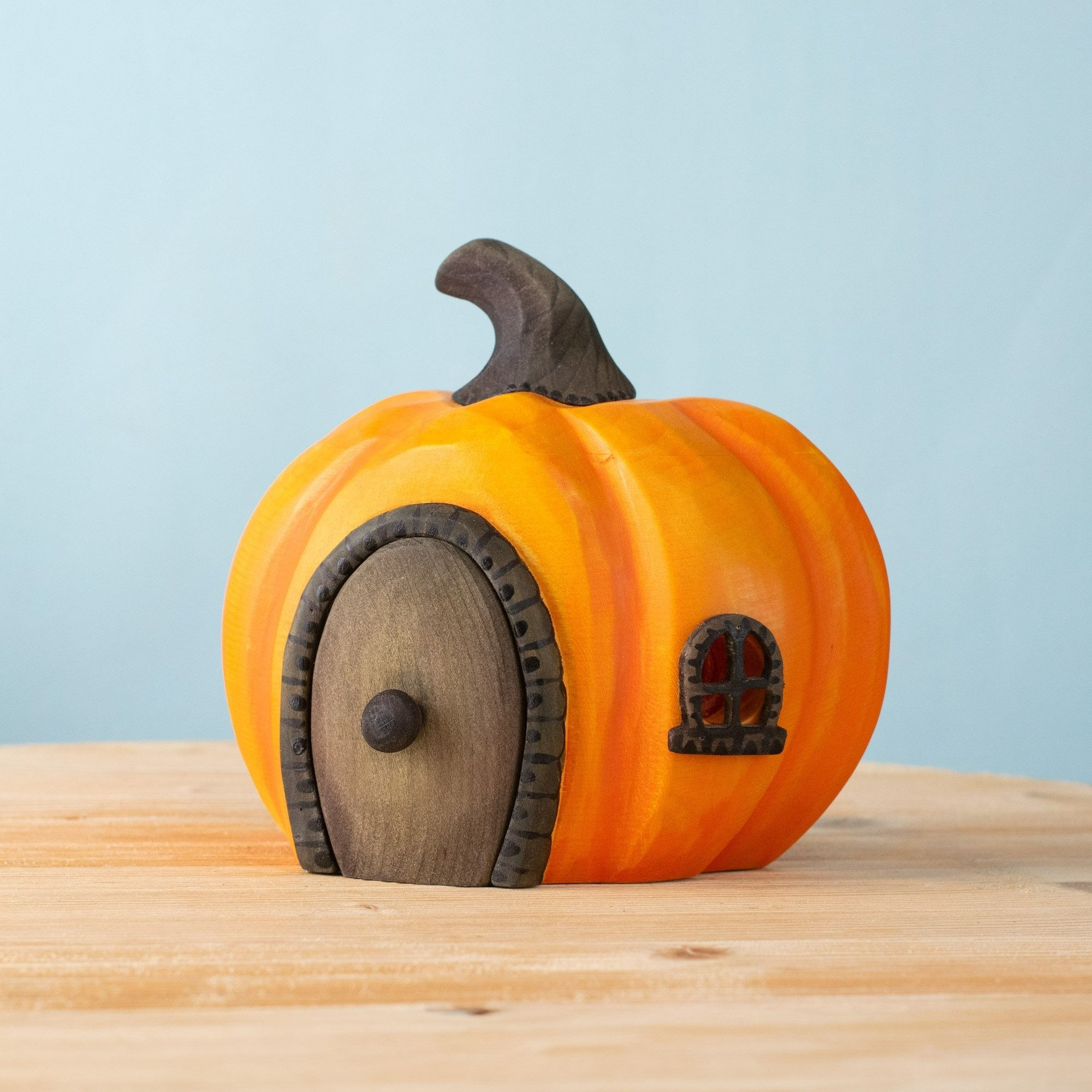 Hand carved wooden Halloween pumpkin house by Bumbu Toys, painted in deep orange with carved windows for autumn and seasonal