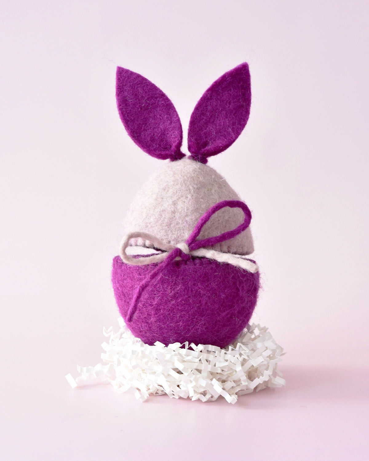 Purple felt bunny ear Easter egg cover by Tara Treasures resting on white paper grass