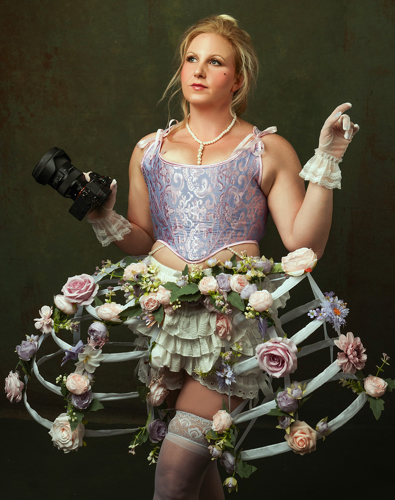 A person dressed in a whimsical, floral-themed costume featuring a lavender corset, hoop skirt adorned with artificial flower