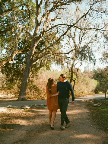 A couple walking together in Pease Park looking at eachother with their arms around eachother.