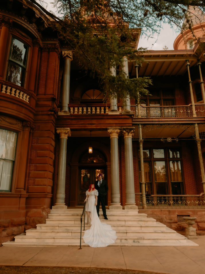 A bride and groom standing on a staircase in front of the Littlefield House on the UT Campus