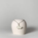 Pingente em porcelana com formato de um veleiro, minimalista, inspirado em origami, a dobradura japonesa. Apoiado sobre um copo branco.