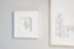 Quadro com fundo branco e moldura branca, com uma delicada folha de porcelana também branca. Instalada ao lado de outro quadro na parede.