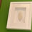 Miniatura: Quadro com fundo branco e moldura branca, com uma delicada folha de porcelana também branca. Instalada numa parede verde.