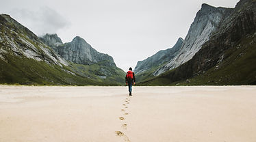Man with backpack walking away alone at sandy beach in mountains Travel lifestyle concept