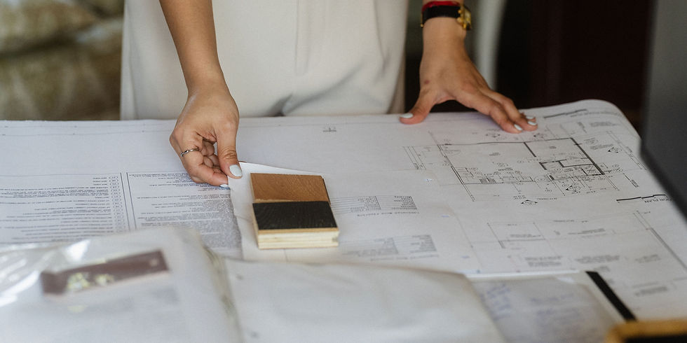 Hands examining architectural plans on a desk with wood samples. Background is blurred; mood is focused and professional.