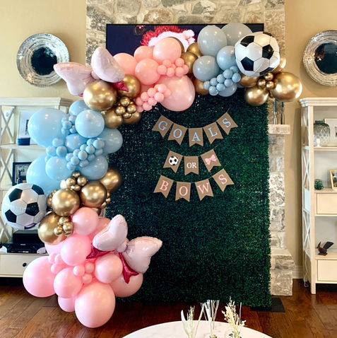 Grass wall backdrop with pink and blue balloon garland for gender reveal party